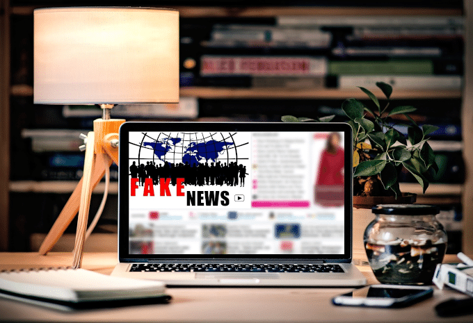 A laptop on a computer desk displaying "fake news"